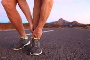Male Runner Holding Ankle in Pain on Desert Road